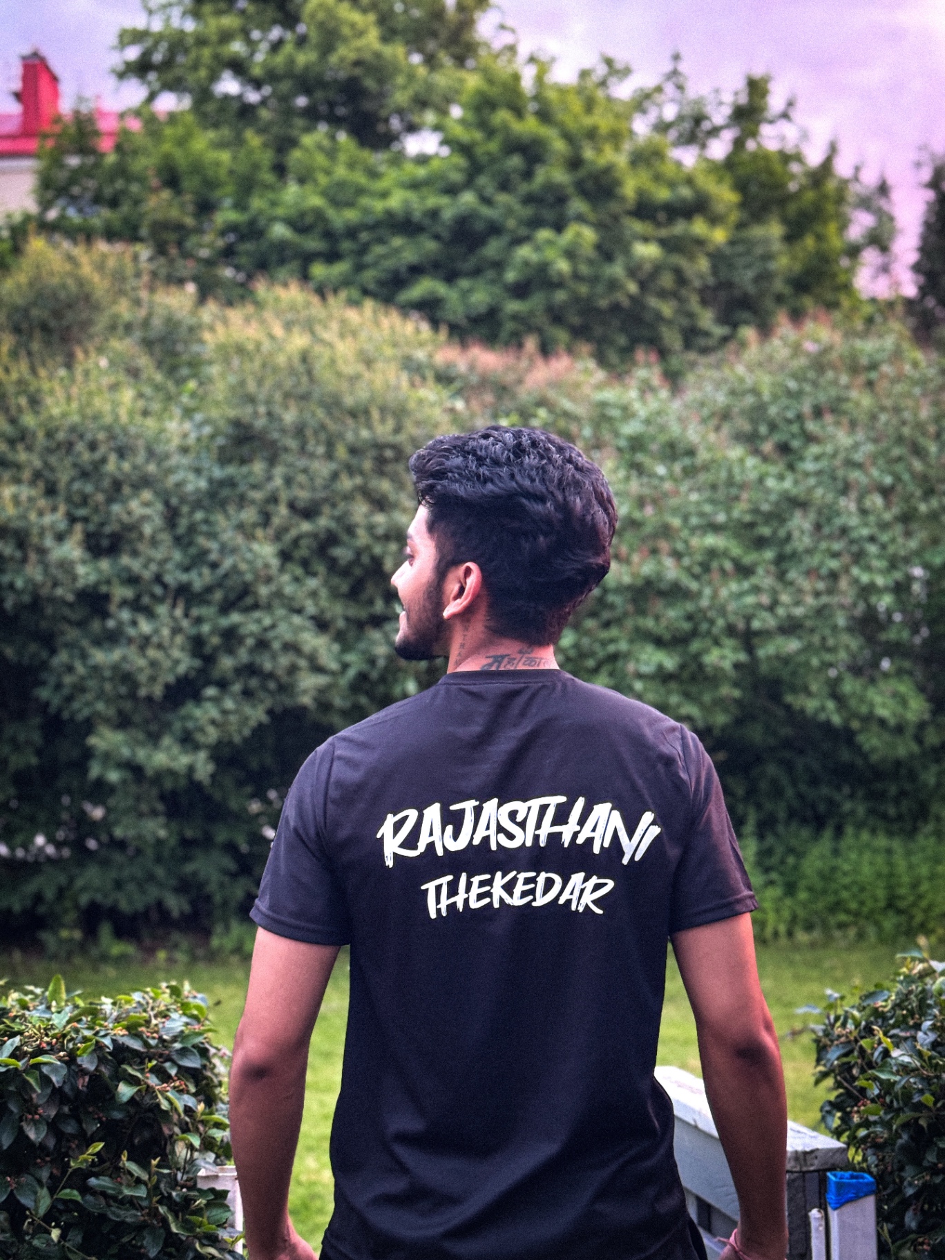 Back of a black t-shirt with RAJASTHANI THEKEDAR hand-painted in white brush lettering